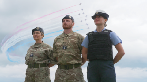 Three reservists in uniform with the red arrows flying past behind. 