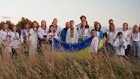 Group of Ukrainian adults and children wearing traditional embroidered clothing and holding Ukrainian flags in a field.