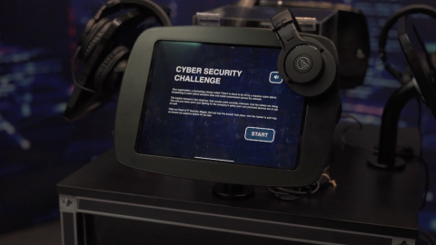 Tablet displaying an interactive cyber security challenge, with headphones and other equipment arranged around it.
