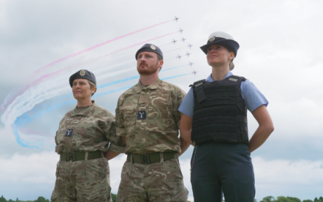 Three reservists in uniform with the red arrows flying past behind. 