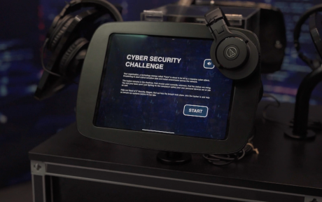 Tablet displaying an interactive cyber security challenge, with headphones and other equipment arranged around it.